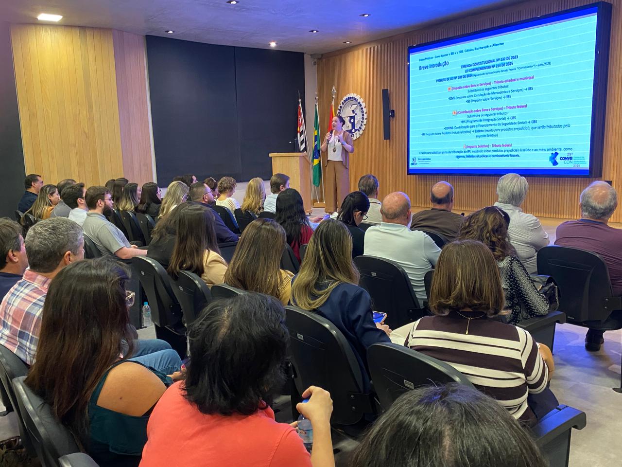 Prof.ª Danieli Aragão ao púlpito — slide IBS/CBS Breve Introdução · CONVECON · jul 2025